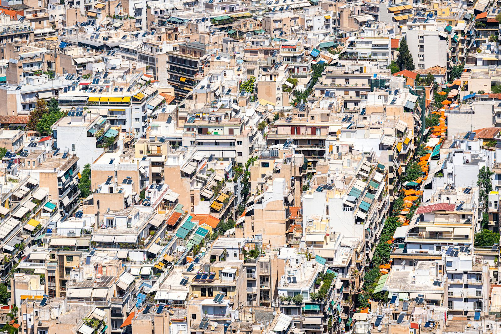 Athens seen from above: dense apartment blocks, roof terraces, solar heaters and a street of orange awnings running through the middle.